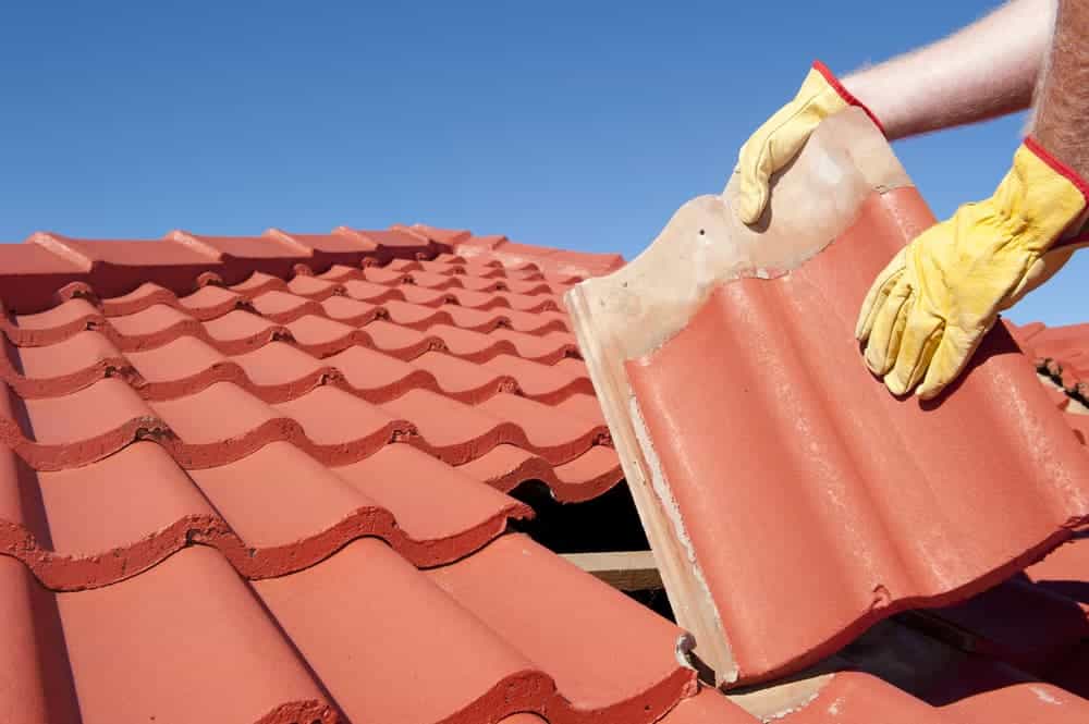 Gloved hands lifting a red concrete roof tile during a tile roof repair