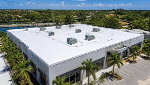 Aerial view of an office building with a new white flat roof surrounded by palm trees