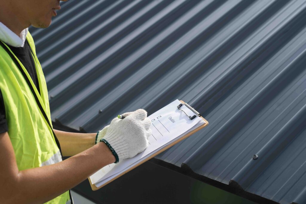Roof inspector in a safety vest filling out a checklist on a dark metal roof