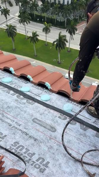 Roofer applying foam adhesive to set terracotta tiles along a roof edge