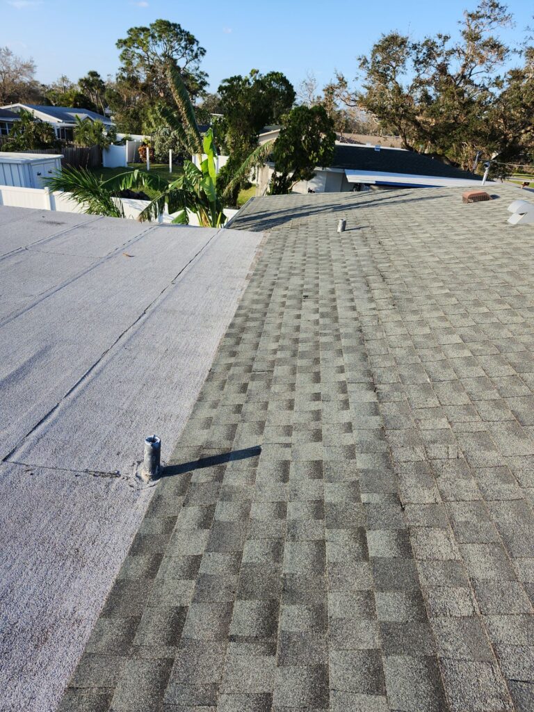 Residential roof with a gray flat roof section beside architectural asphalt shingles
