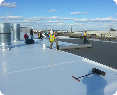 Crew rolling out a white single-ply membrane during a warehouse roof replacement