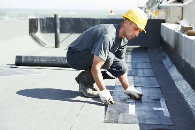 Roofer in a hard hat sealing seams of a bitumen membrane on a flat roof